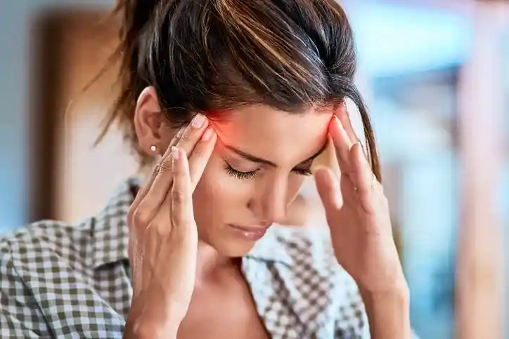 Woman holding her temples with a headache and exhaustion caused by low thyroid hormone
