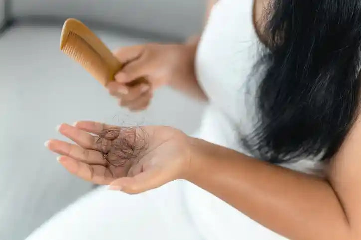 Woman holding a comb and a handful of hair shed from thyroid-related hair loss