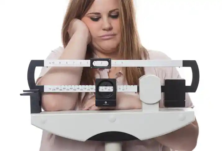Woman leaning on a medical scale, discouraged by unexplained thyroid-related weight gain